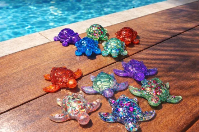 Ten glitter resin turtles in different colourways beside a pool
